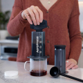 AeroPress Original Kaffeezubereiter – Kaffee wird in der Küche direkt in eine Glastasse gepresst, mit Zubehör daneben
