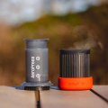 Préparation du café avec l’AeroPress® Go en plein air – presse à café et tasse posées sur une table en bois.


