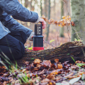 Personne préparant du café avec l’AeroPress® Go dans la forêt – préparation sur une souche lors d'une sortie nature.


