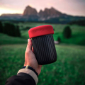 AeroPress® Go tenue à la main devant un paysage de montagne – machine à café de voyage compacte.


