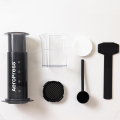 Ensemble complet de l'AeroPress Coffee & Espressomaker - XL sur fond blanc, incluant une carafe, des filtres en papier, une cuillère doseuse et une spatule.



