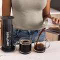 Une personne verse du café fraîchement infusé d'une carafe dans deux tasses à côté d'une AeroPress Coffee & Espressomaker - XL.


