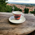 Tasse à espresso Aquarelli avec un motif d'arbre et de coucher de soleil sur une table en bois dans un village italien.