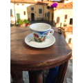 Tasse à café Aquarelli avec un motif de fleurs (coquelicots et bleuets) sur une table en bois dans un village italien.


