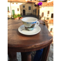 Tasse à café Aquarelli avec un motif de lac et de paysage sur une table en bois dans un environnement méditerranéen.


