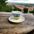 Tasse à espresso Aquarelli avec un motif de paysage sur une table en bois dans un environnement méditerranéen.