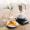 Hario Dripper Kasuya présenté sur une table avec une carafe et des croissants.


