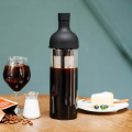 Bouteille Hario Cold Brew Coffee Filter, 650 ml, remplie de café infusé à froid, posée sur une table en bois avec un verre de café et un gâteau.


