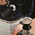Hario Porte-filtre à café V60 Kasuya pendant le versement d’eau avec une bouilloire, sur une balance pour une précision optimale.


