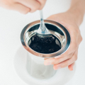 Gros plan du remplissage du filtre du Slow Drip Brewer HARIO SHIZUKU avec une cuillère.


