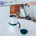 Vue rapprochée d'une carafe Hario V60 blanche servant du café chaud dans un verre.


