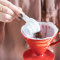 Hario V60 Messlöffel 12g Weiss beim Einfüllen von Kaffeepulver in roten V60 Handfilter