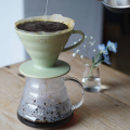 Hario V60 en porcelaine Smokey Green sur une carafe en verre pendant l'extraction du café.


