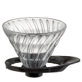 Porte-filtre à café Hario V60 en verre, taille 02 pour 1-4 tasses, sur un sous-verre noir, montrant la structure en spirale unique, idéal pour la préparation du café filtre.

