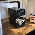 Beanarella Nori black coffee machine on a wooden countertop in a camper, with a cup under the spout and stacked books beside it.


