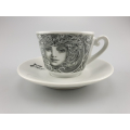 Monochrome Liberty Kaffeetasse mit einem Gesicht im Jugendstil auf weisser Untertasse, verbindet traditionelle Motive mit modernem Stil.