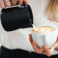 Barista versant du lait avec le pichet à lait Rhinowares Stealth pour réaliser un latte art dans une tasse à cappuccino.