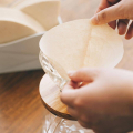 Une personne plie un filtre papier brun naturel Hario V60 avant de l'insérer dans un porte-filtre.