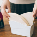 Une main prend un filtre papier Hario V60 de la boîte, prêt à être utilisé pour la préparation du café.
