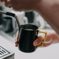 Barista hält Milchkännchen mit gelbem Rhino Silikon Griffüberzug 32oz beim Milchschäumen