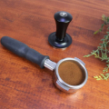 Tamper auto-nivelant Rhino, 58 mm, accompagné d’un porte-filtre, station café en arrière-plan.


