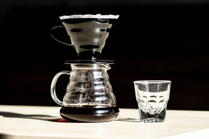 Hario V60 Range Server aus Glas mit einem schwarzen Hario V60 Kaffeefilterhalter, ergänzt durch ein passendes Glas. Perfekt für die Zubereitung von handgefiltertem Kaffee