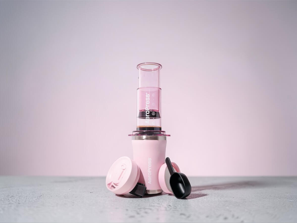 AeroPress Go Plus Travel System pink 15PLPK05 with cup, lid and scoop on light background