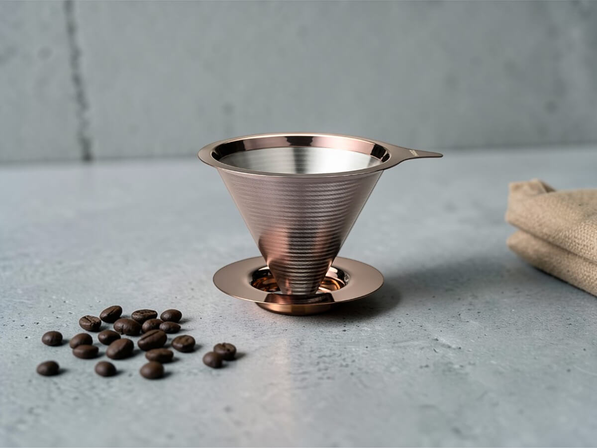Double Mesh Metal Dripper 02 in Pink Gold aus Edelstahl auf hellem Untergrund neben Kaffeebohnen
