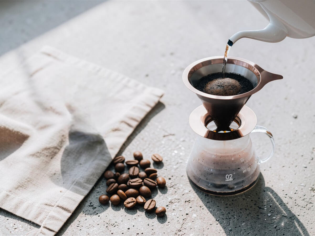 Double Mesh Metal Dripper 02 in Pink Gold aus Edelstahl bei der Handfilter Kaffeezubereitung auf Glaskanne neben Kaffeebohnen
