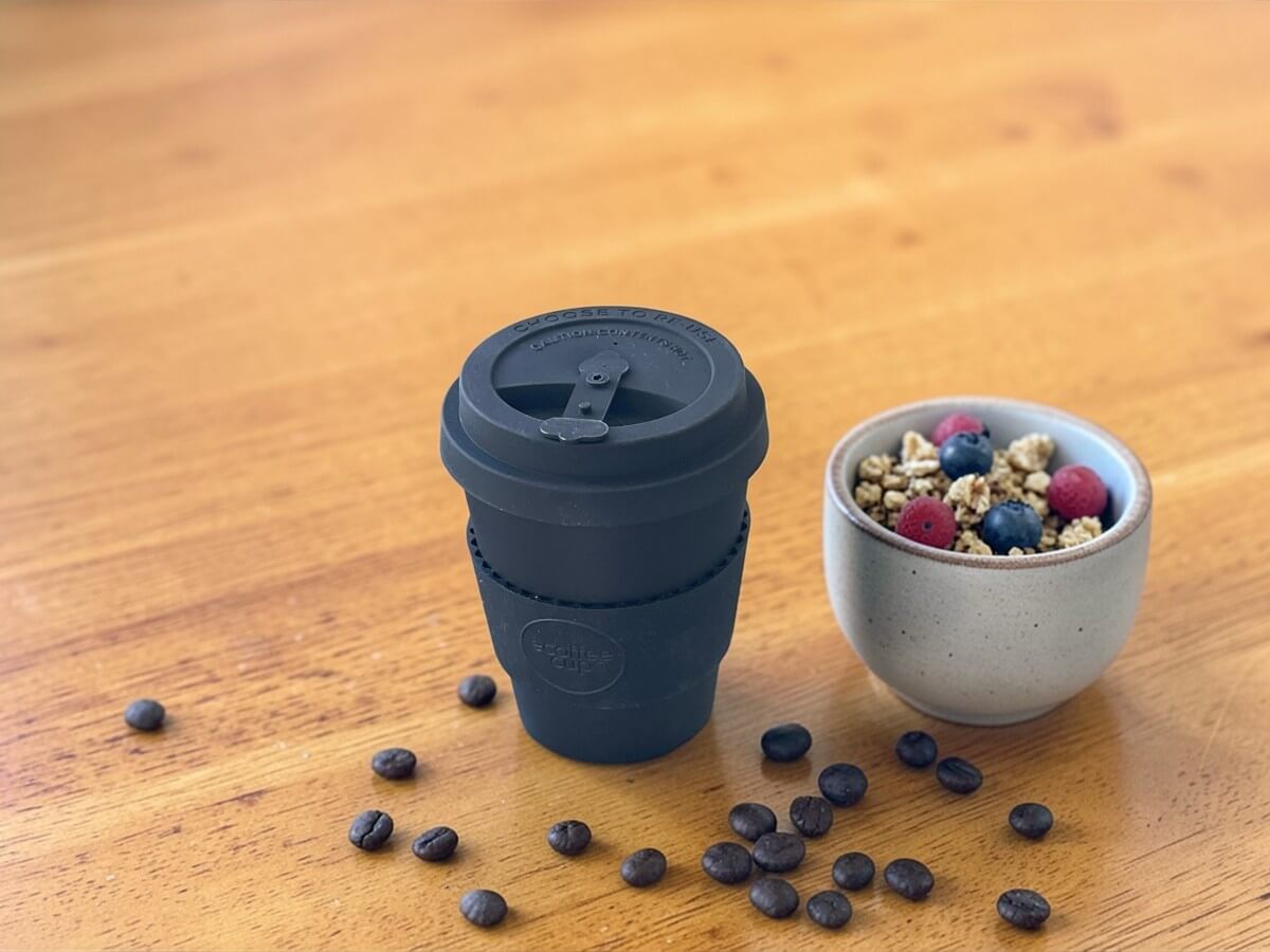 Ecoffee Cup Espressobecher Schwarz 180ml Kerr & Napier auf warmem Holztisch neben Schälchen mit Granola und Beeren und verstreuten Kaffeebohnen im natürlichen Tageslicht