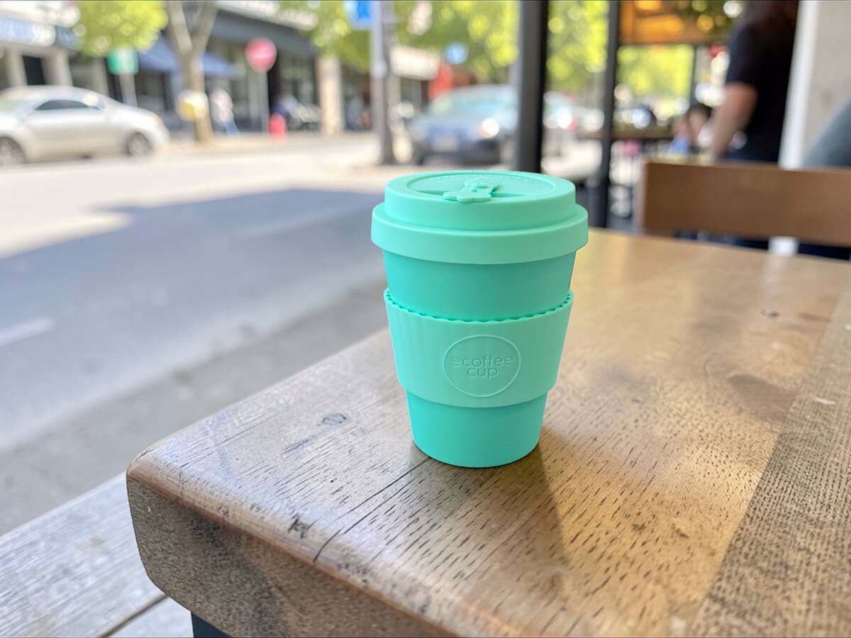 Ecoffee Cup bicchiere riutilizzabile 350ml Grindavik Split in verde menta su tavolo in legno di terrazza caffetteria con vista su strada alla luce del sole