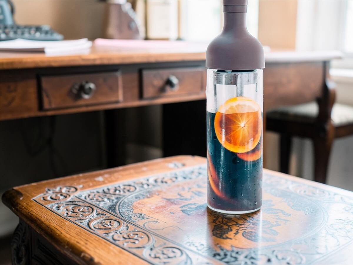 Hario Filter in Coffee Bottle FIC 70 CBR in Chocolate Brown gefuellt mit Cold Brew Kaffee und Orangenscheiben auf Holztisch