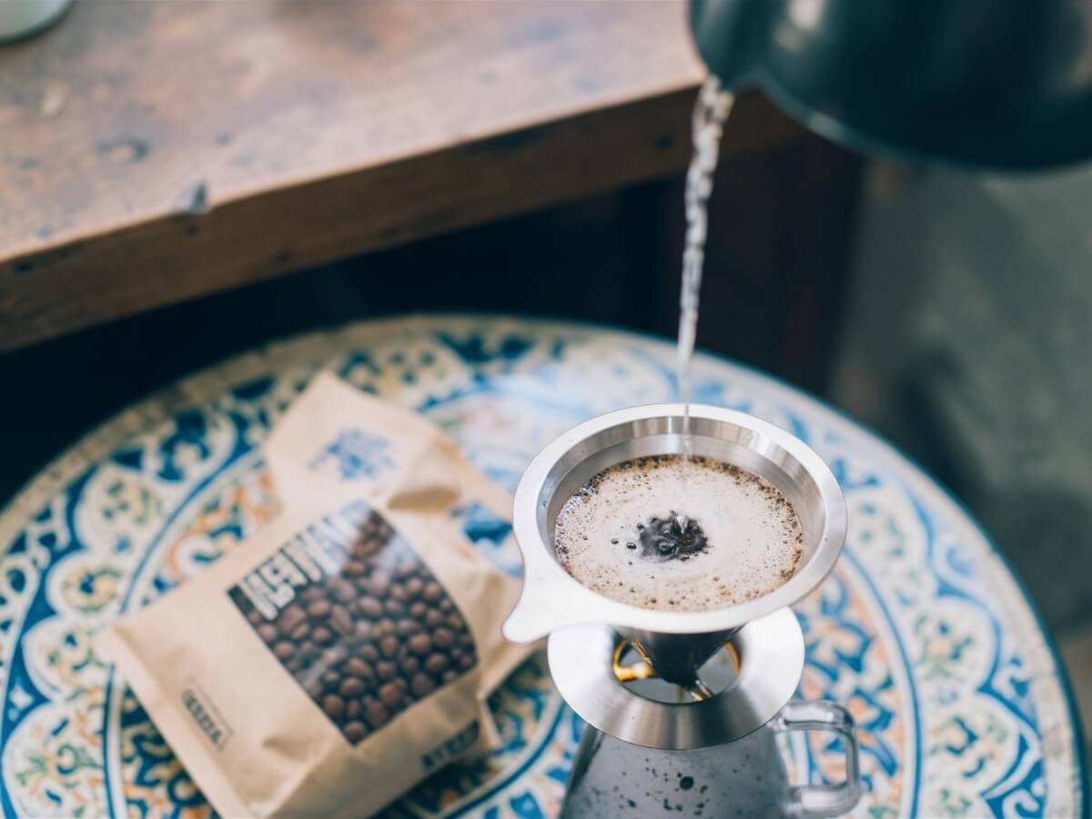 Hario V60 Double Mesh Metallfilter 01 aus Edelstahl beim Handaufguss in Draufsicht mit Kaffeebeutel und Glaskanne