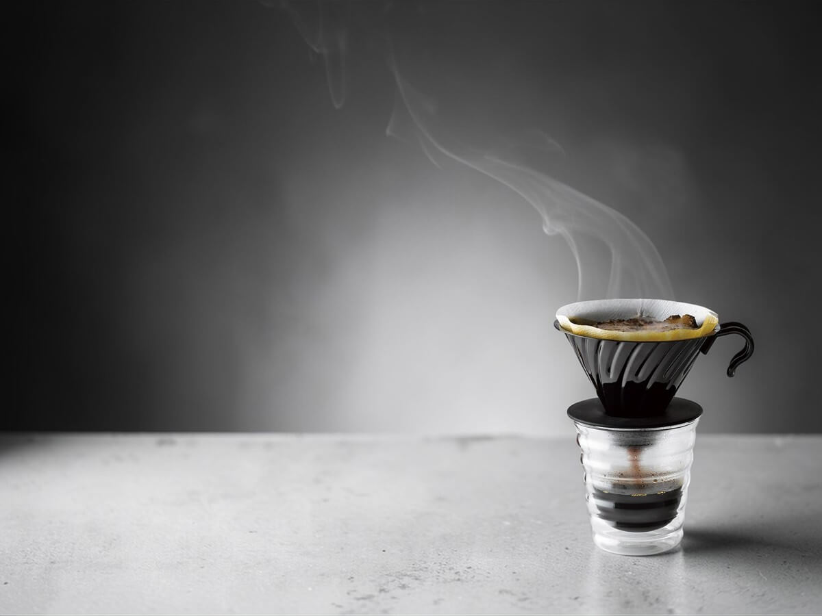 Hario V60 Dripper 02 VDMR 02MB aus Edelstahl mit schwarzer Beschichtung und Silikonbasis beim Handaufguss mit Papierfilter auf Glasbecher