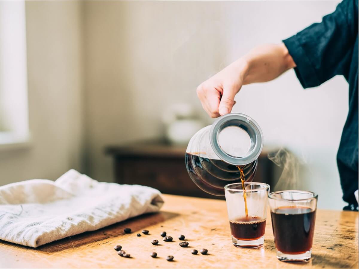 Hario V60 Range Server 800 ml clear glass pouring freshly brewed coffee into two glasses on wooden table