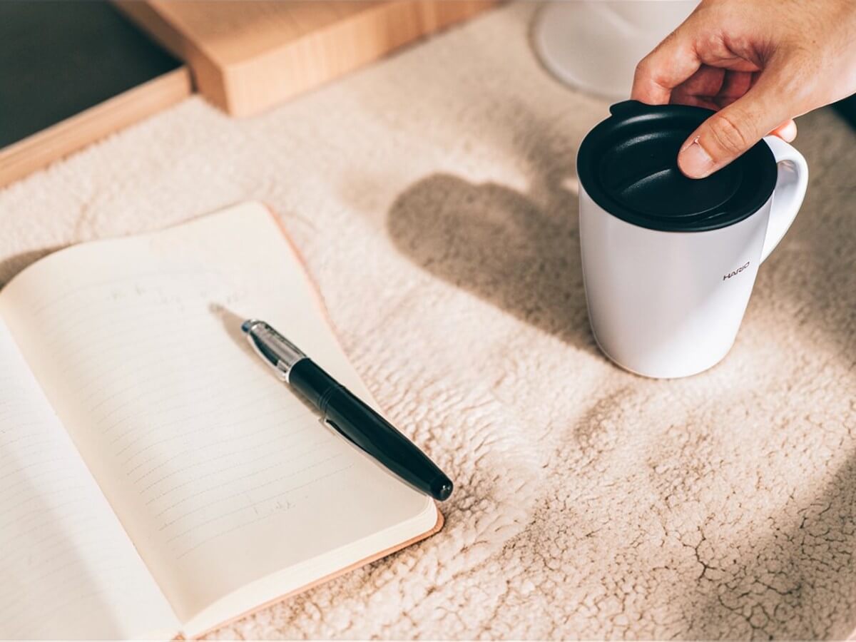 Hario heat retention mug with lid 300 ml grey on desk next to notebook and pen