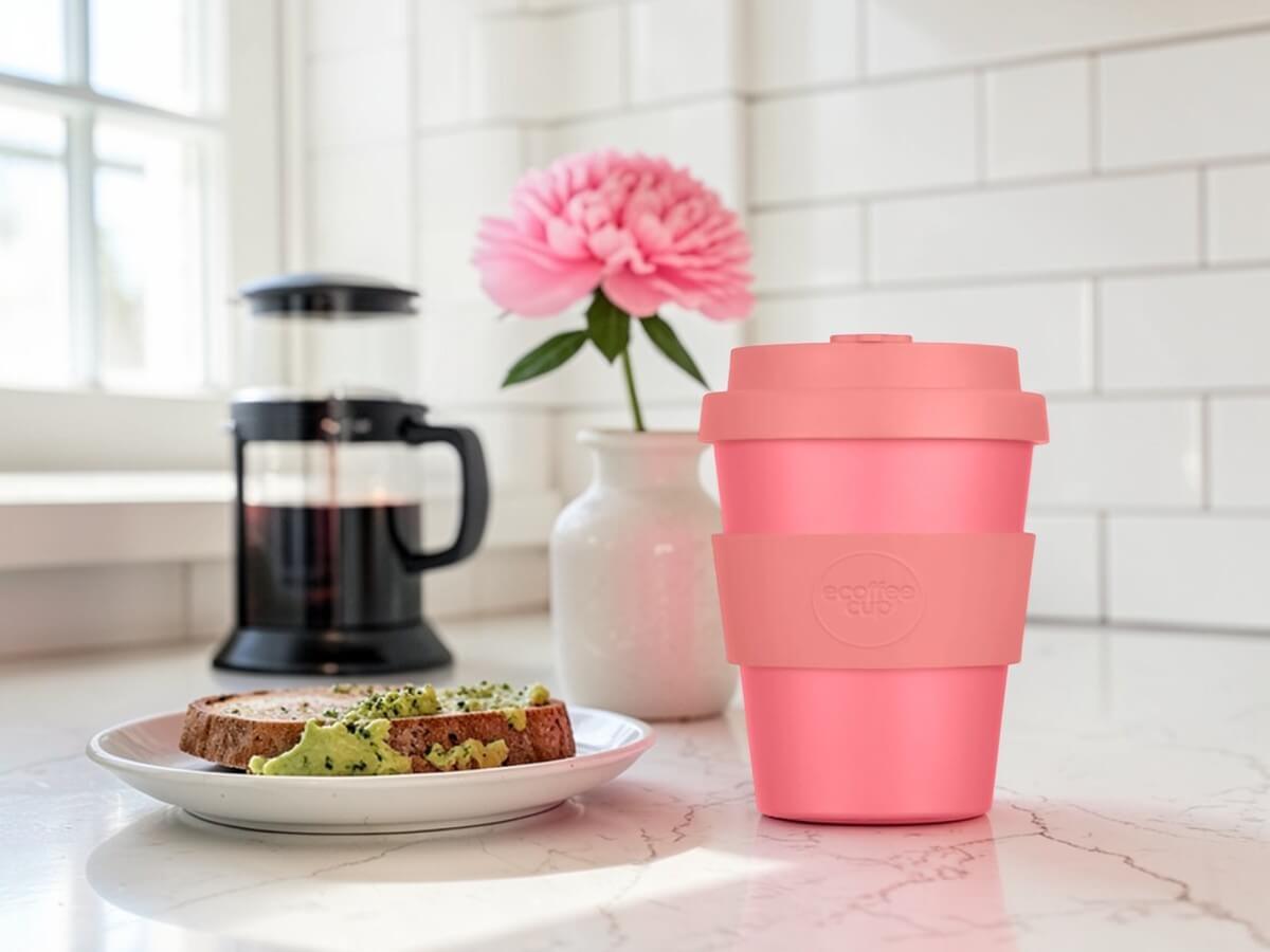 Tazza da caffè in PLA 180ml Darrell Lea Roth su piano da lavoro in marmo con toast avocado caffettiera a stantuffo peonia rosa in vaso di ceramica e piastrelle metro bianche nella luce chiara del mattino