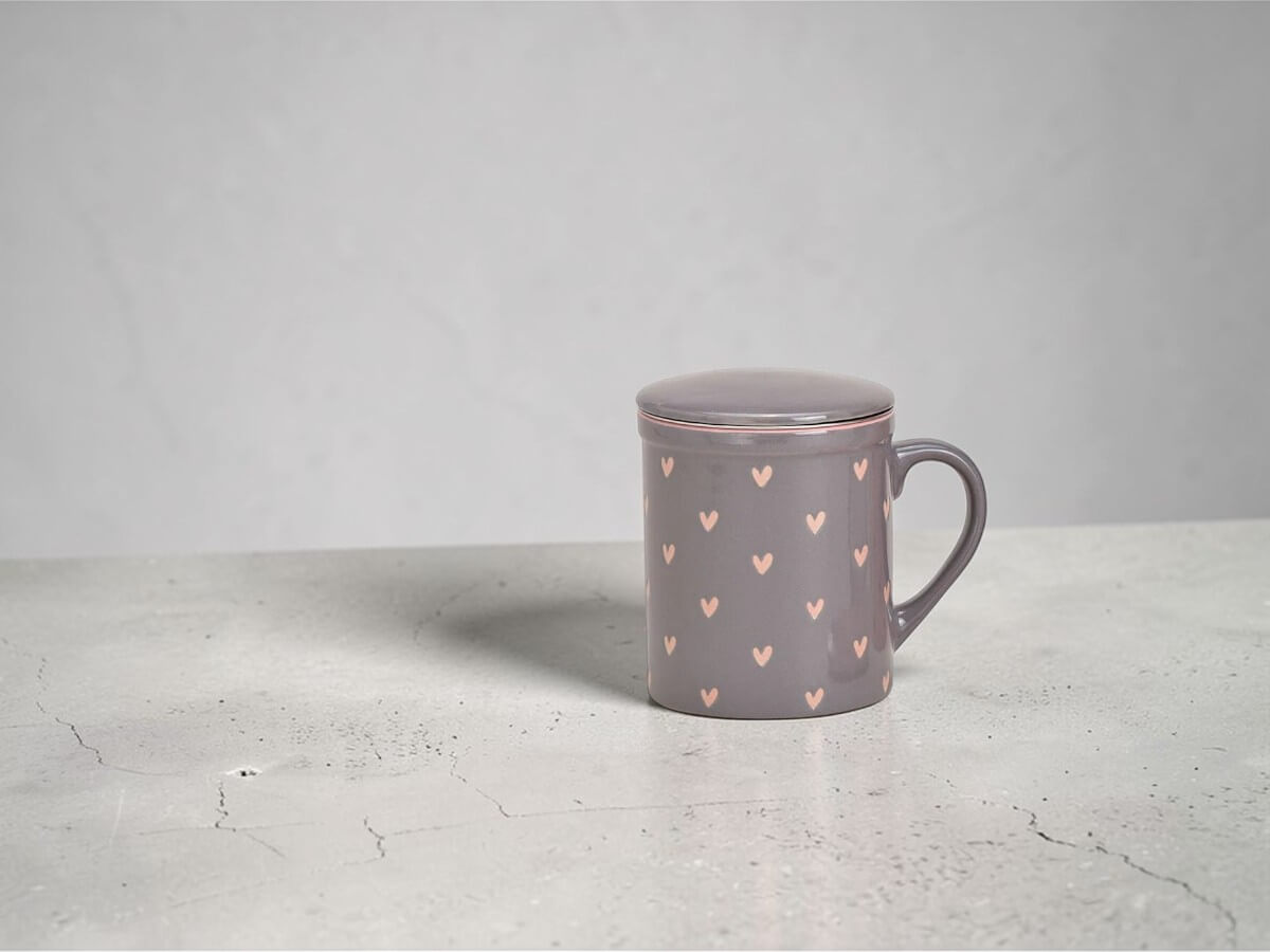 Grauer Keramik Teebecher mit zartem Herz Dekor inklusive Teesieb und Deckel auf neutralem Hintergrund