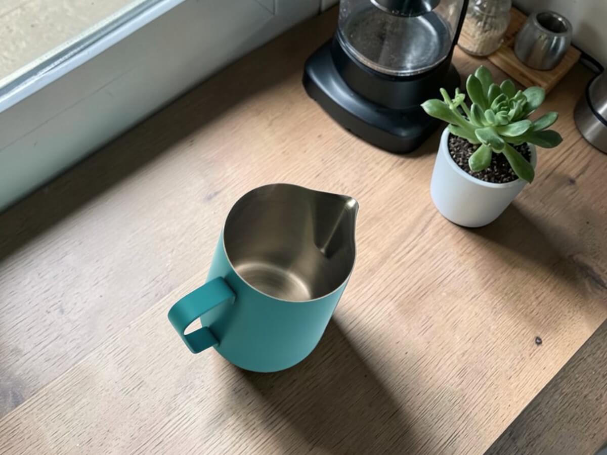 Rhino Classic Milchkanne 450ml in Teal Blue auf Holztisch in Küche neben Kaffeemaschine und Pflanze