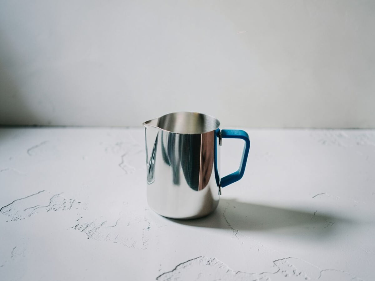 Rhino Blue Silikon Griffüberzug 12oz an Milchkännchen vor hellem Studiohintergrund