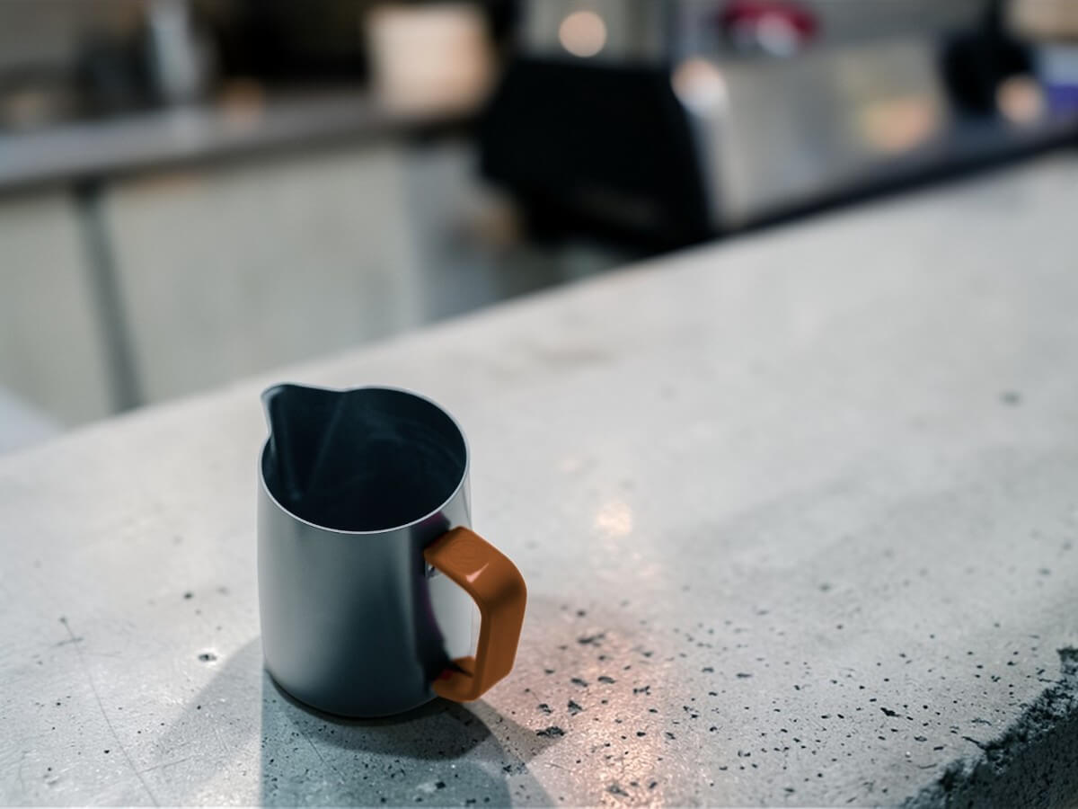 Rhino Brown Silikon Griffüberzug 12oz an Milchkännchen auf Beton-Theke mit Café-Hintergrund