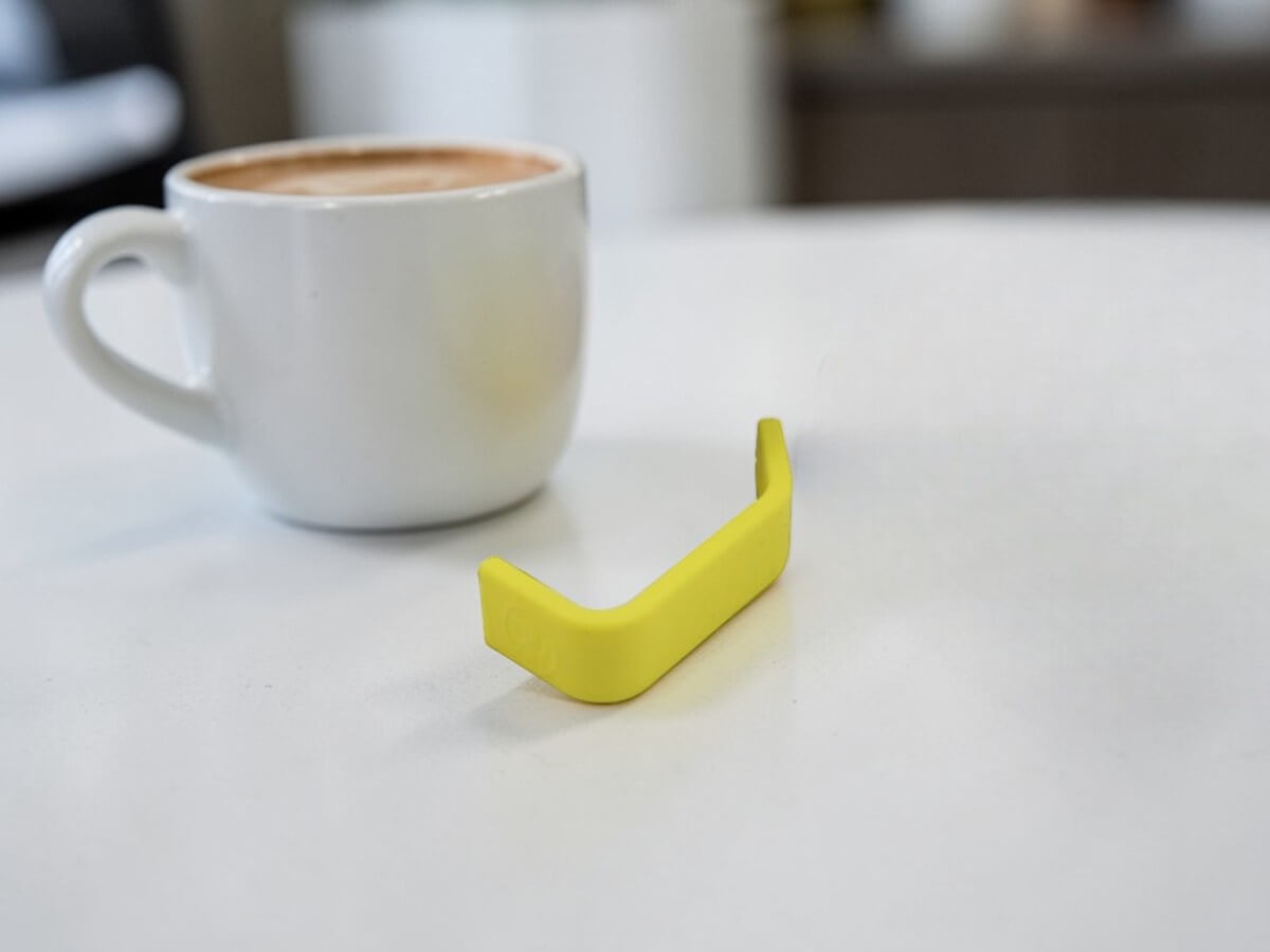 Rhino Yellow Silikon Griffüberzug 12oz auf Tisch mit Kaffeetasse im Hintergrund