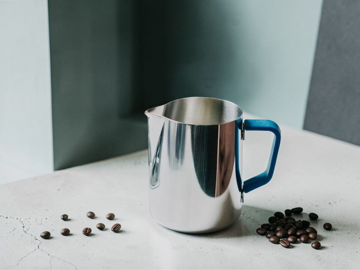 Rhino Blue Silikon Griffüberzug 32oz an Milchkännchen auf Betonoberfläche mit Kaffeebohnen