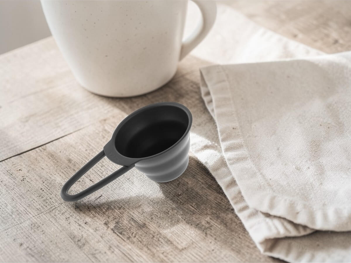V60 Messlöffel 12g in Matt Schwarz auf Holztisch neben Tasse und Leinentuch